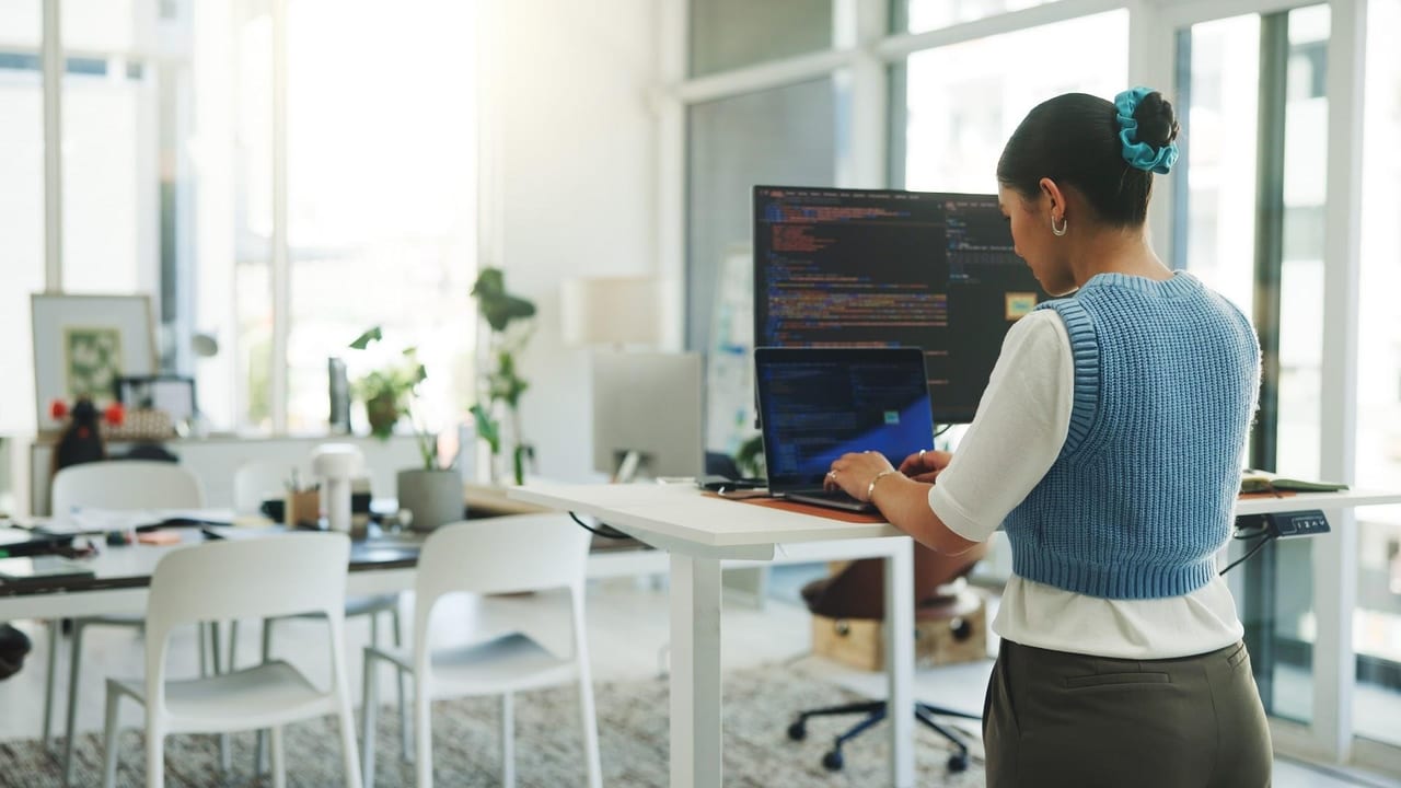 A developer working at a standing desk, code open across a monitor and a laptop.